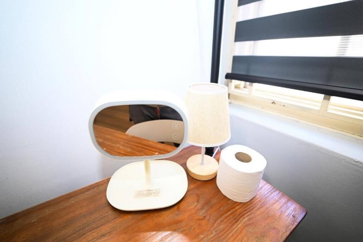 A bedside table with a mirror, a lamp, and a roll of toilet paper.