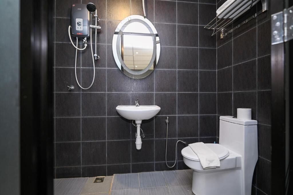 Une salle de bain moderne avec un mur recouvert de carreaux noirs, un lavabo blanc, des toilettes et une douchette à main.