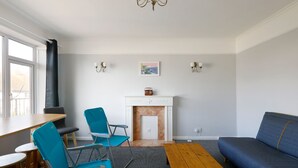 A modern living room with a fireplace, two blue chairs, a wooden coffee table, and a sofa. - Spacious 2-Bedroom Flat Near Rottingdean Beach & Windmill (Brighton and Hove)