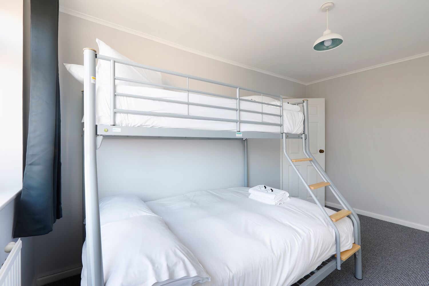 A bunk bed with a ladder, white bedding, and a ceiling light fixture.