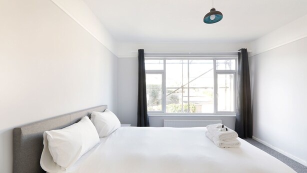 A hotel room with a large bed, a window with curtains, and a ceiling light. - Spacious 2-Bedroom Flat Near Rottingdean Beach & Windmill (Brighton and Hove)