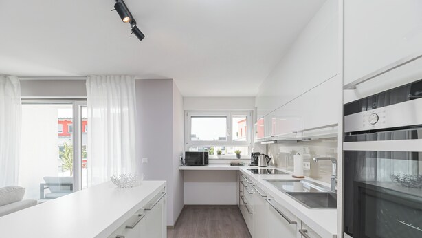 A modern kitchen with white cabinetry, a large island, a microwave, and an oven.