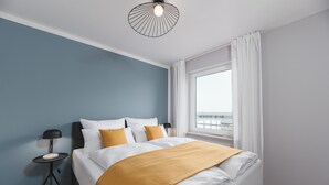 A hotel room with a bed, a side table with a lamp, a window with curtains, and a view of the outside.