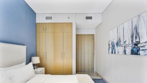 Ein modernes Hotelzimmer mit einem großen Bett, einem Holzschrank, einem Gemälde mit Segelbooten und einer blauen Akzentwand.