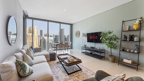 Ein modernes Wohnzimmer mit großem Fenster, einer Couch, einem Couchtisch, einem Fernseher und einem Bücherregal.