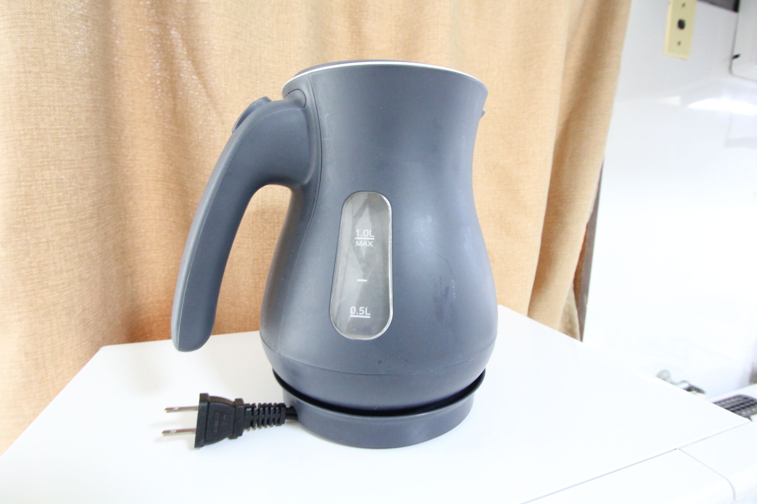 A gray electric kettle with measurement markings on its side, placed on a white surface.
