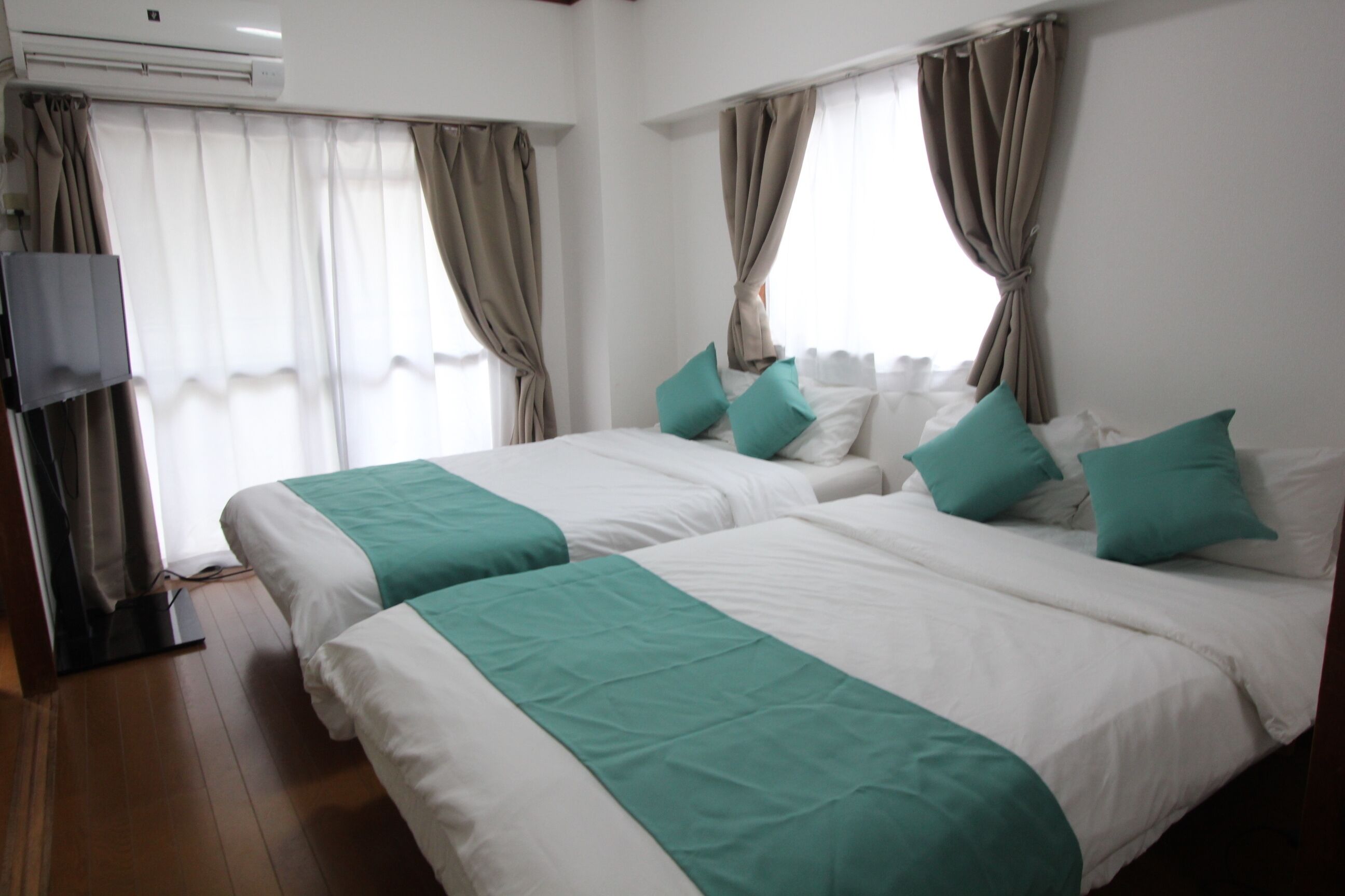 A hotel room with two beds, beige curtains, white bedding, and a flat-screen TV.