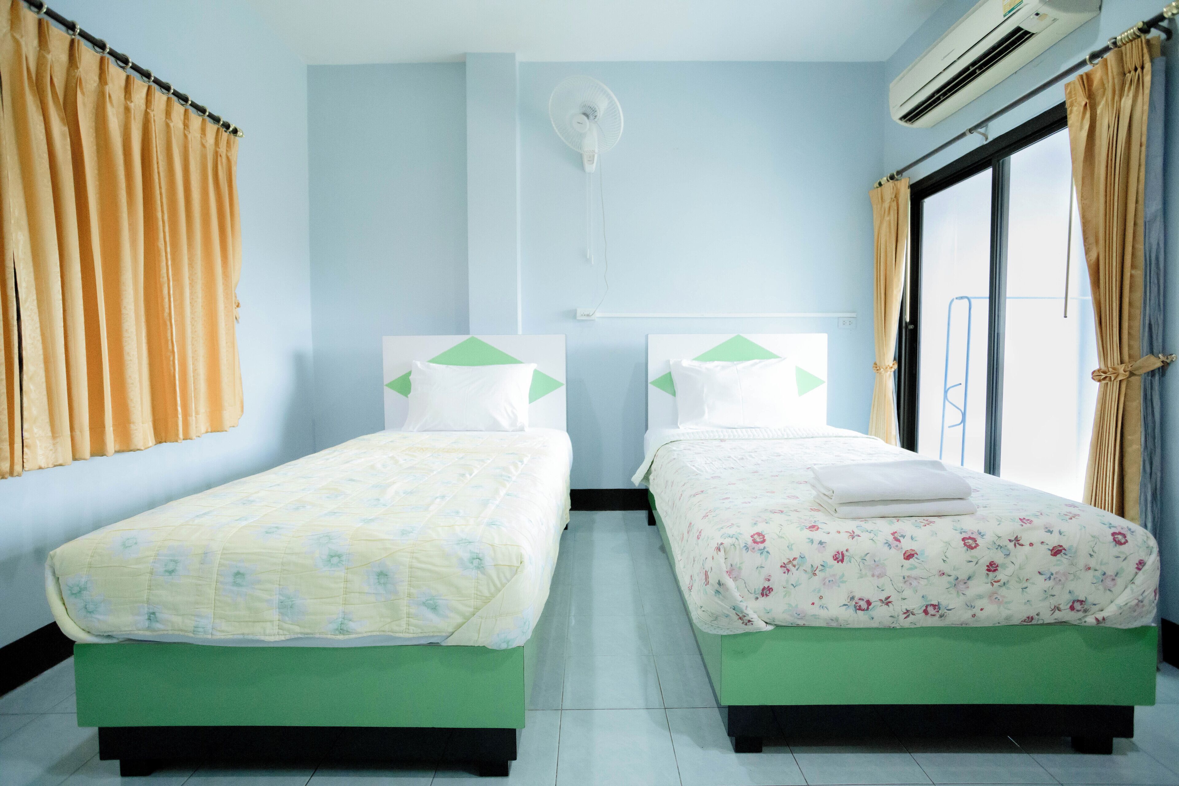 Habitación con dos camas, cada una con una almohada y una toalla doblada. Se ve un ventilador de techo y un equipo de aire acondicionado.