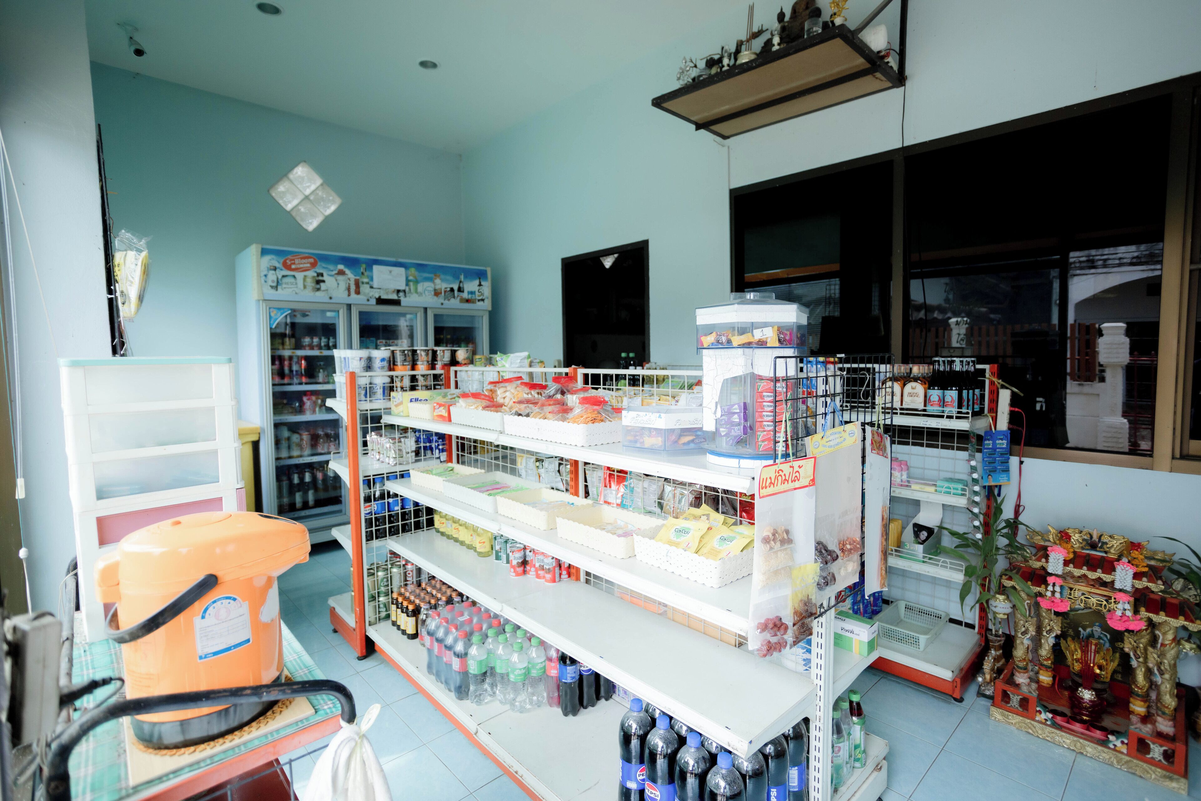 Uma farmácia com prateleiras repletas de produtos diversos, um refrigerador e uma exposição de água engarrafada.