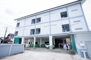 A multi-story building with a covered parking area and a small adjacent structure with a sink. - Thongkon Hotel (Surin)