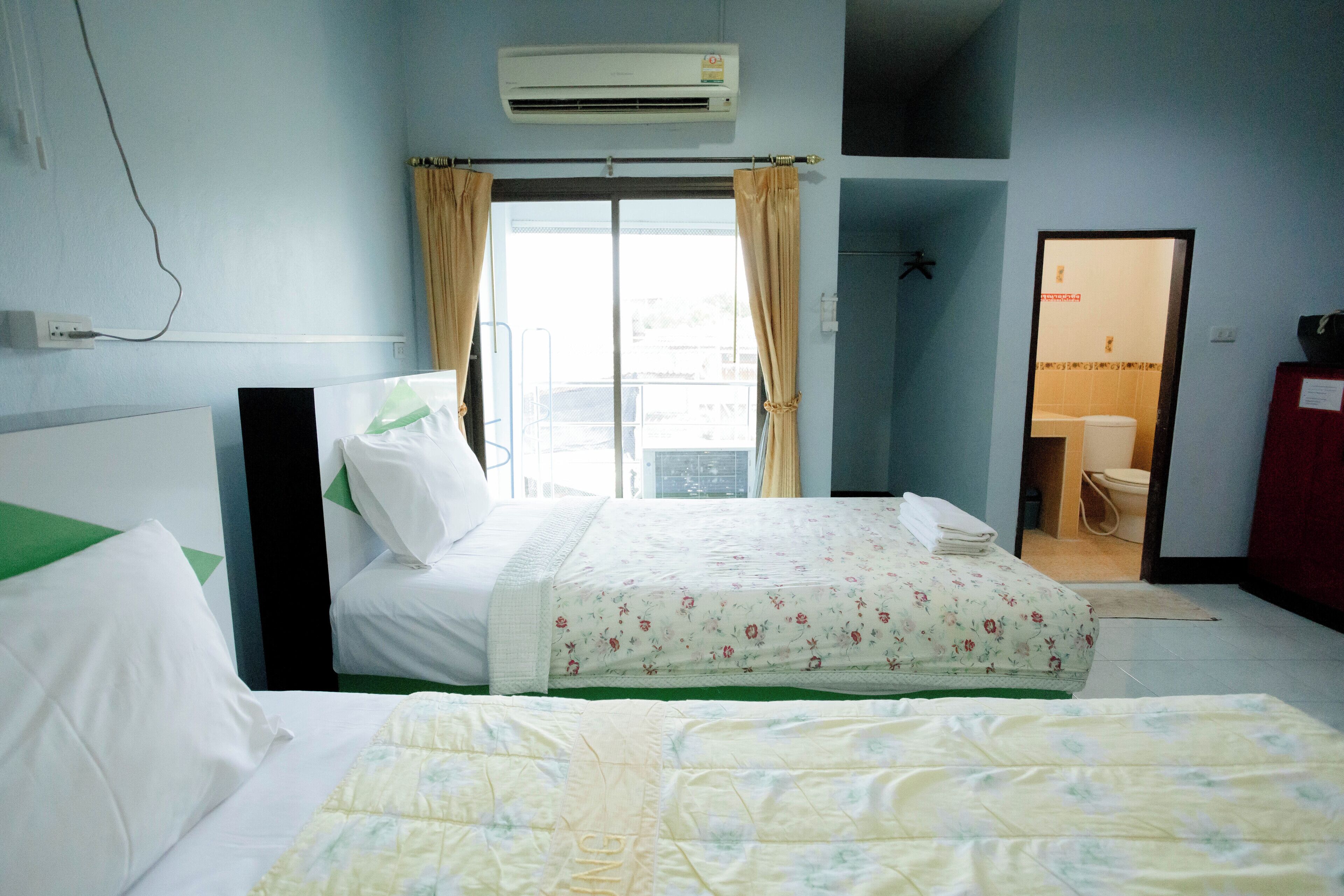 Une chambre d’hôtel avec un lit, une fenêtre avec des rideaux, un climatiseur et une vue sur l’extérieur.