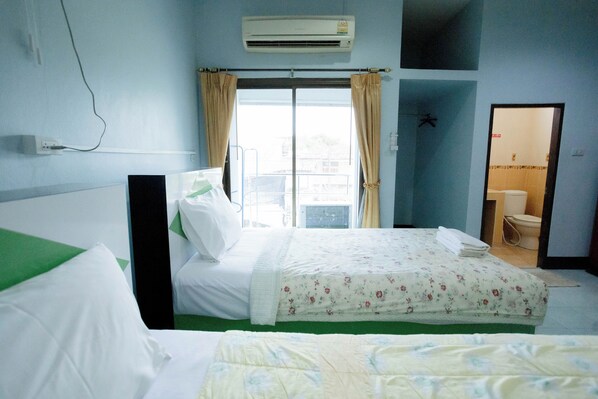 Habitación de hotel con dos camas, ventana con cortinas, aire acondicionado y baño visible a través de una puerta abierta.