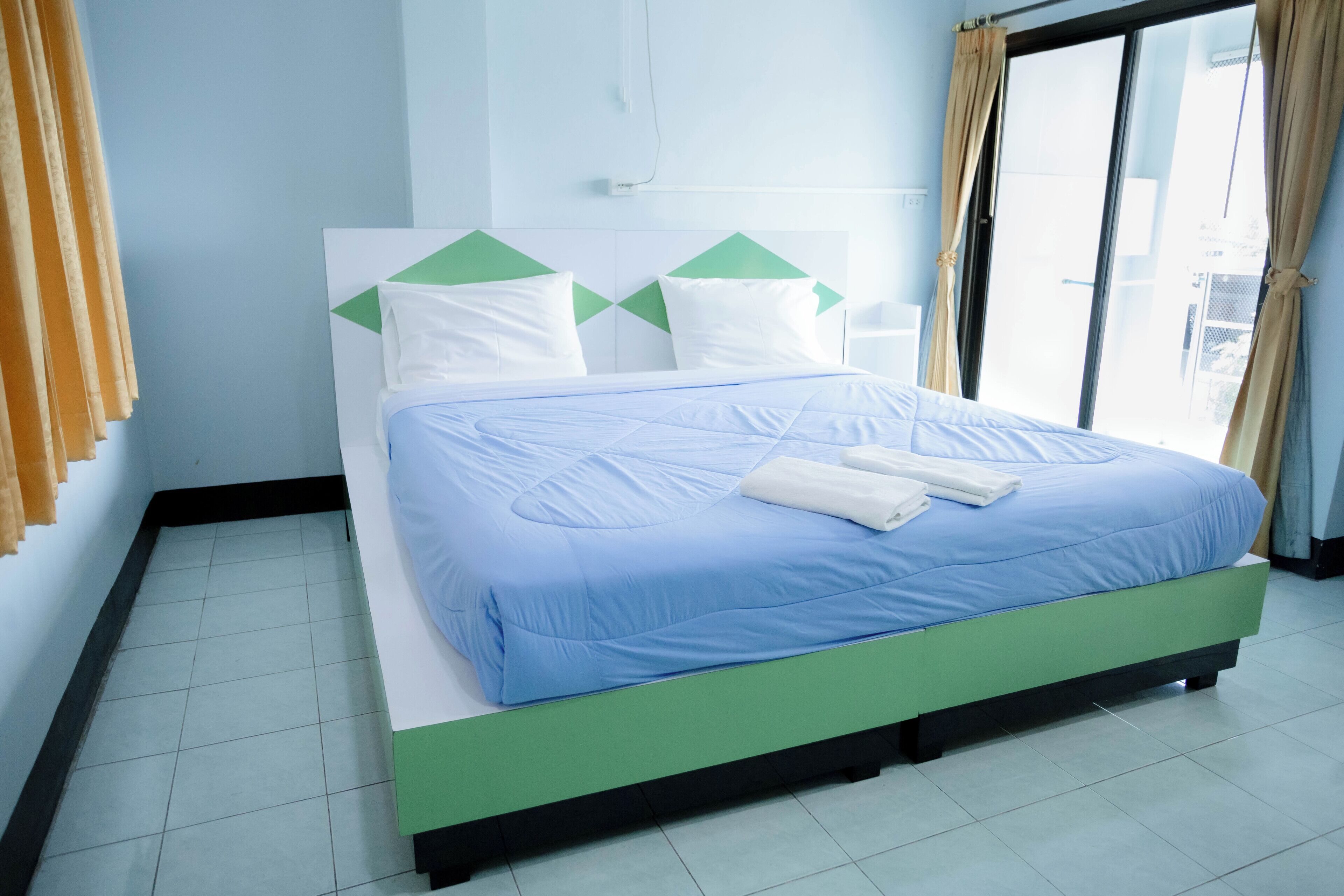 A neatly made bed with a blue and white bedspread, a green headboard, and white pillows.