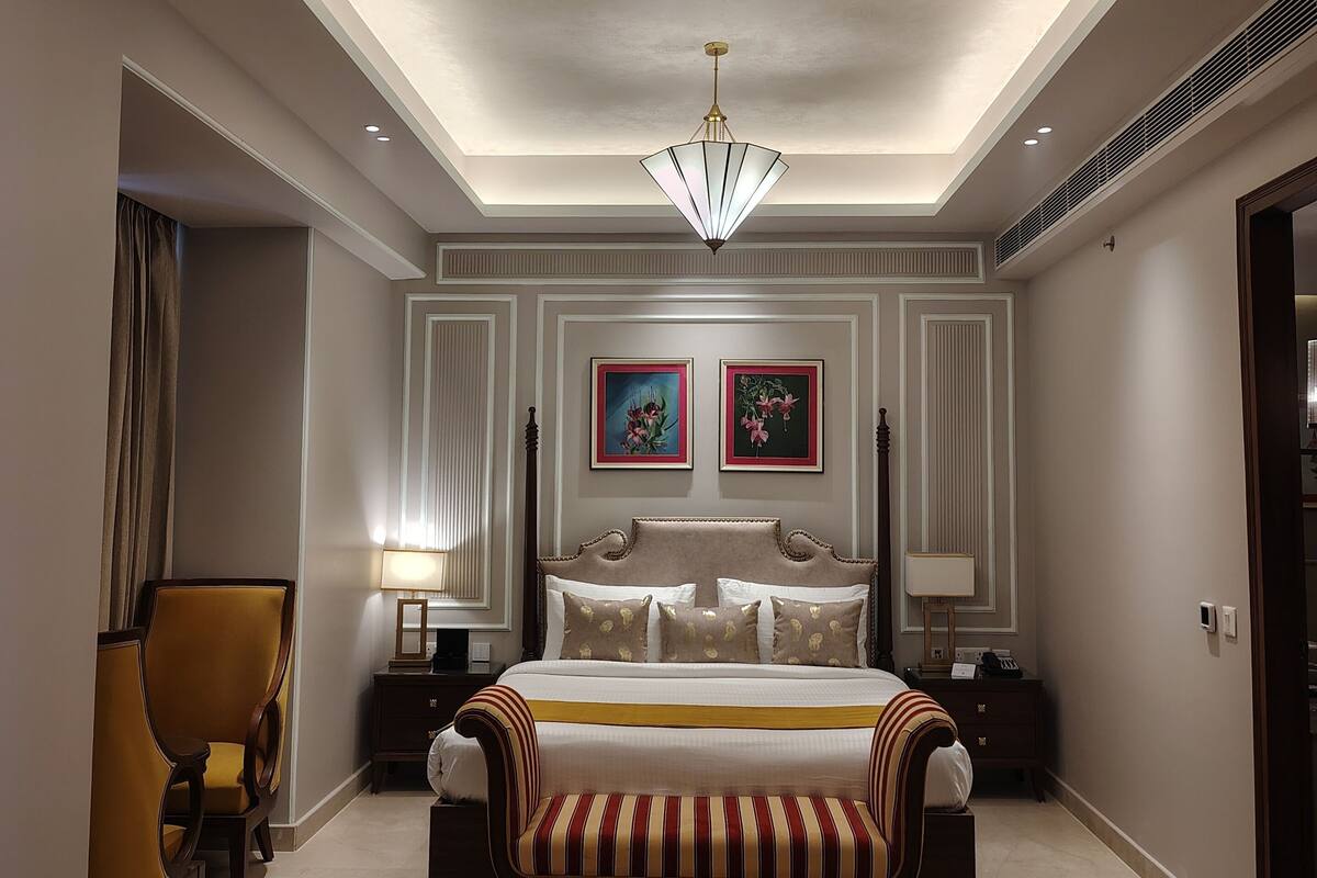 A hotel room with a large bed, a chandelier, a nightstand, a chair, and two framed pictures on the wall.
