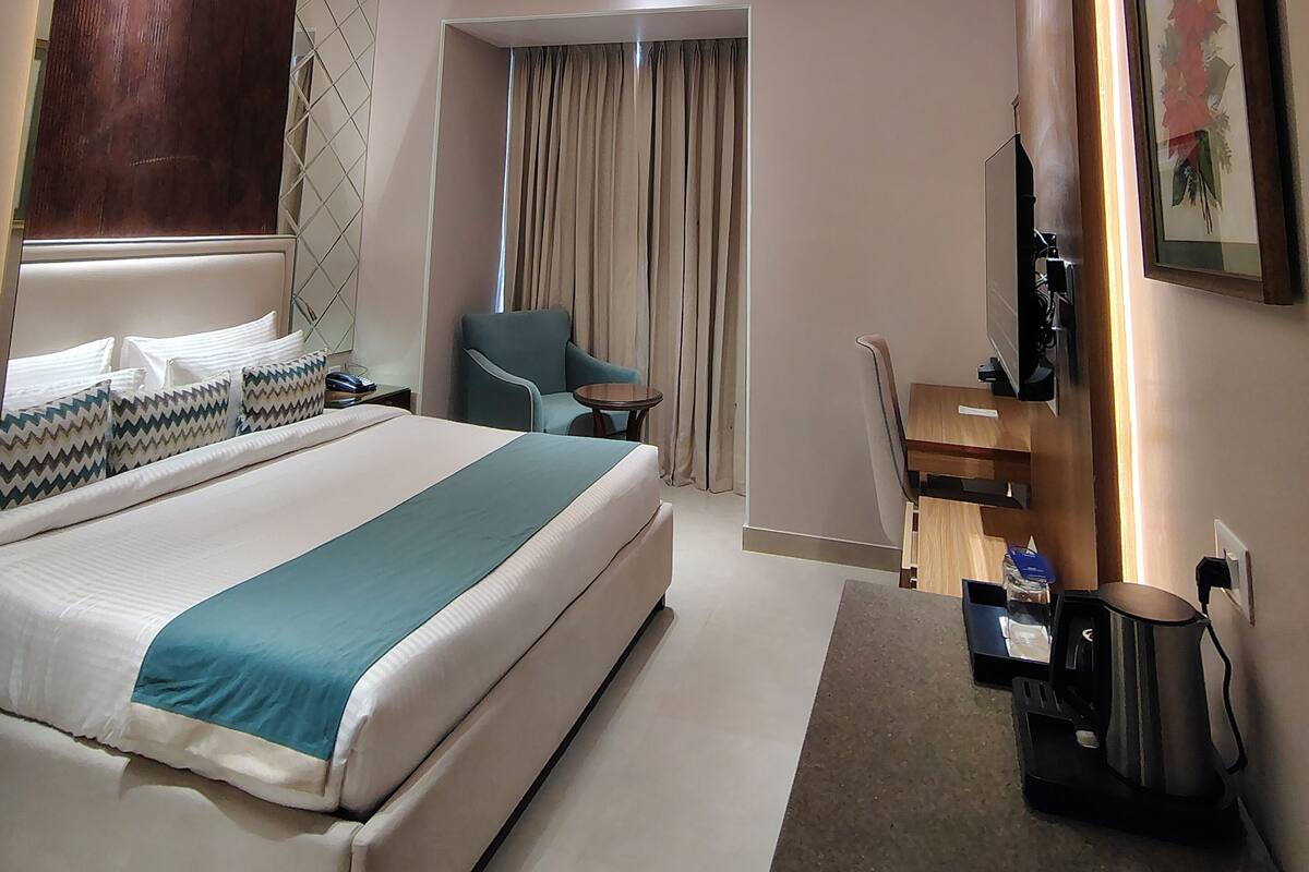 A modern hotel room with a large bed, a desk, a chair, and a television.