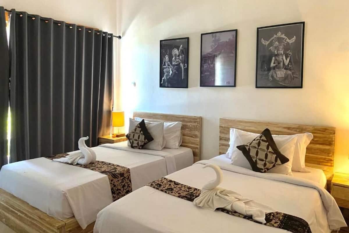 Habitación de hotel con dos camas, cada una con colcha blanca y almohadas decorativas con forma de cisne. Hay cuadros enmarcados en la pared y una ventana con cortinas.