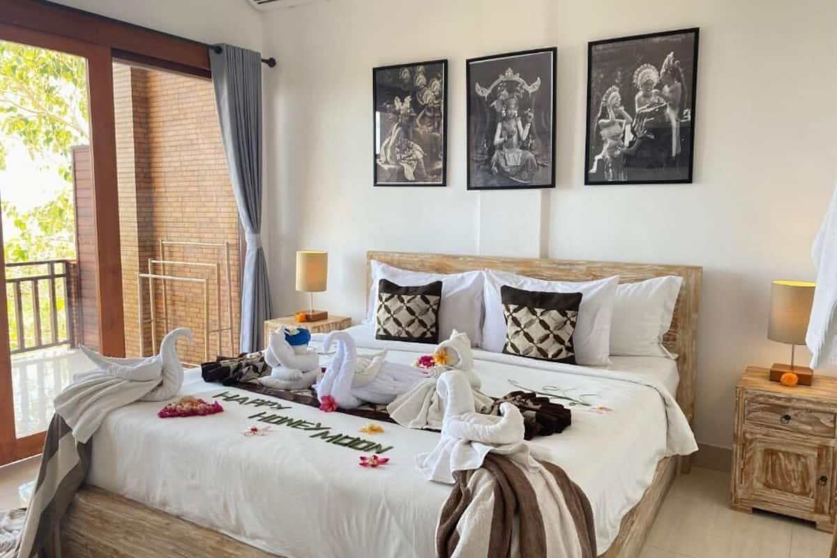 Una habitación de hotel con una cama grande, dos almohadas, una mesita de noche, una ventana con cortinas y decoración en la pared.