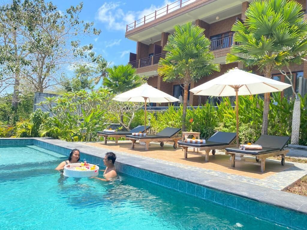 A swimming pool with lounge chairs and umbrellas, surrounded by lush greenery and a building with balconies.