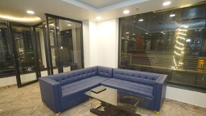 Un sofá seccional azul con una mesa de centro de vidrio en un interior moderno con piso de mármol y ventanas amplias.