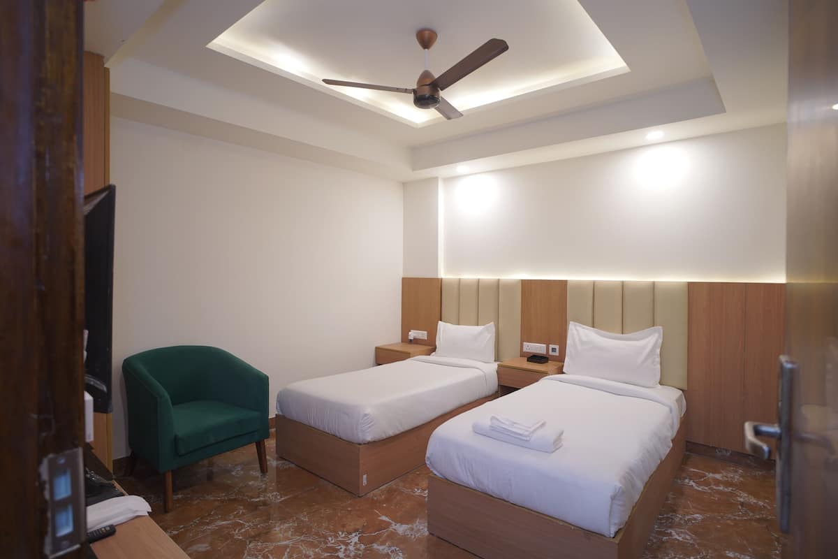 Une chambre d’hôtel avec deux lits, un fauteuil vert, un ventilateur de plafond et une télévision.