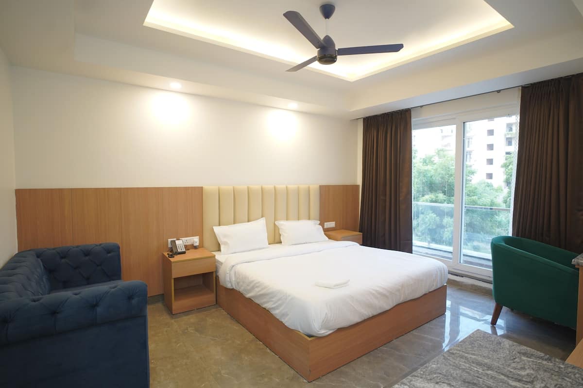 Une chambre d’hôtel moderne avec un grand lit, un bureau, un fauteuil bleu et un fauteuil vert.