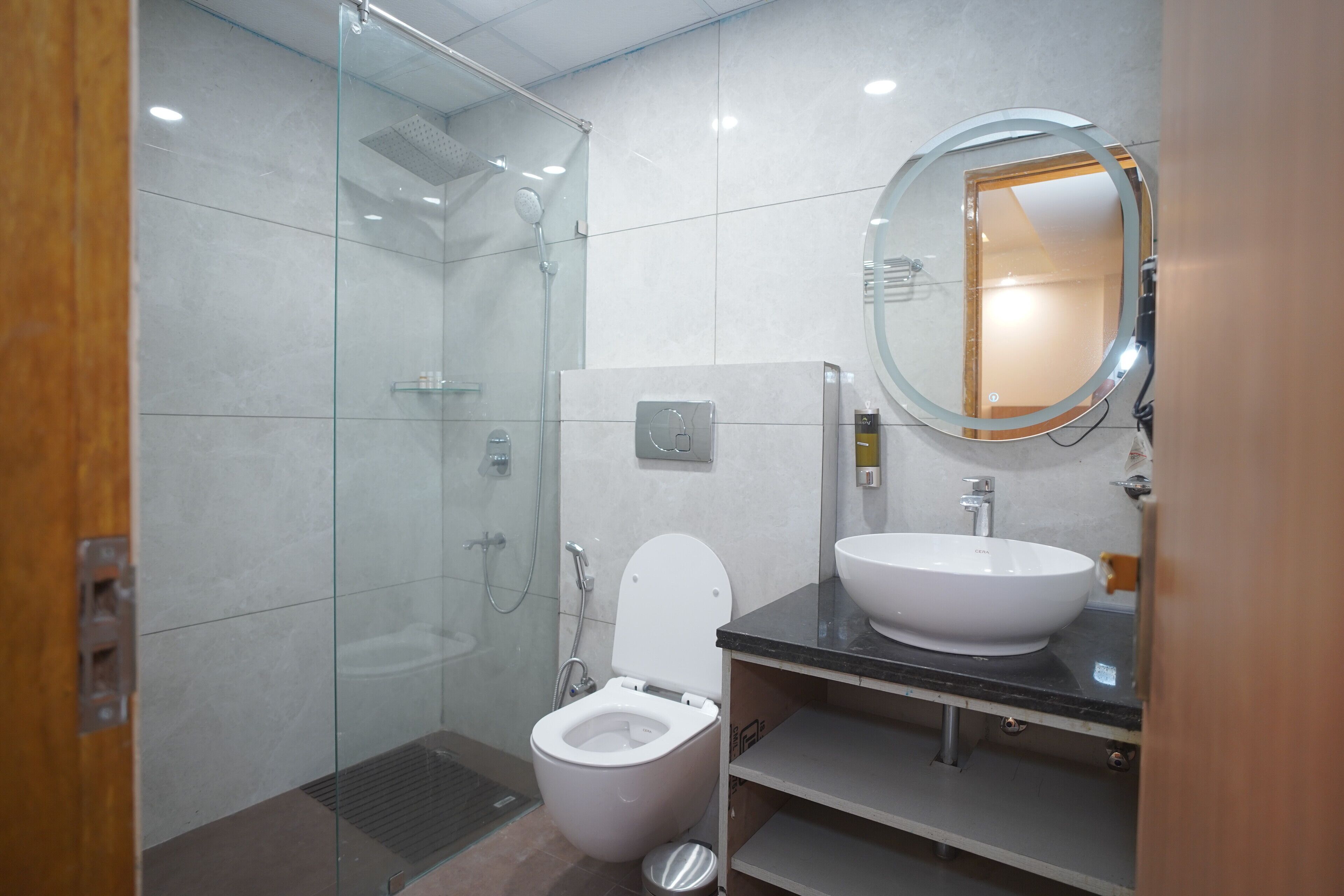 A modern bathroom with a glass-enclosed shower, a white toilet, and a round mirror above a sink.