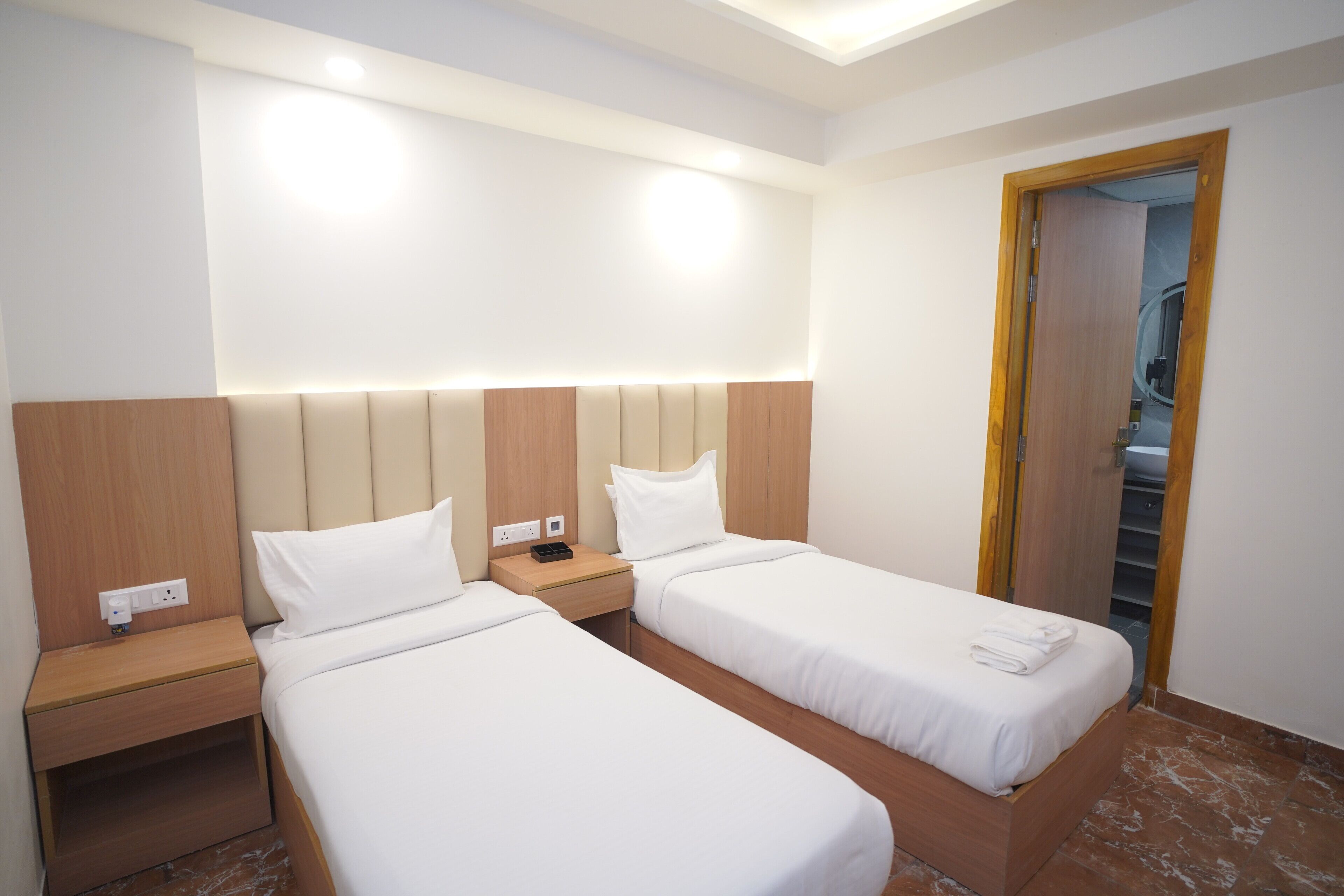 A hotel room with two single beds, wooden headboards, a nightstand with a phone, and a door leading to a bathroom.