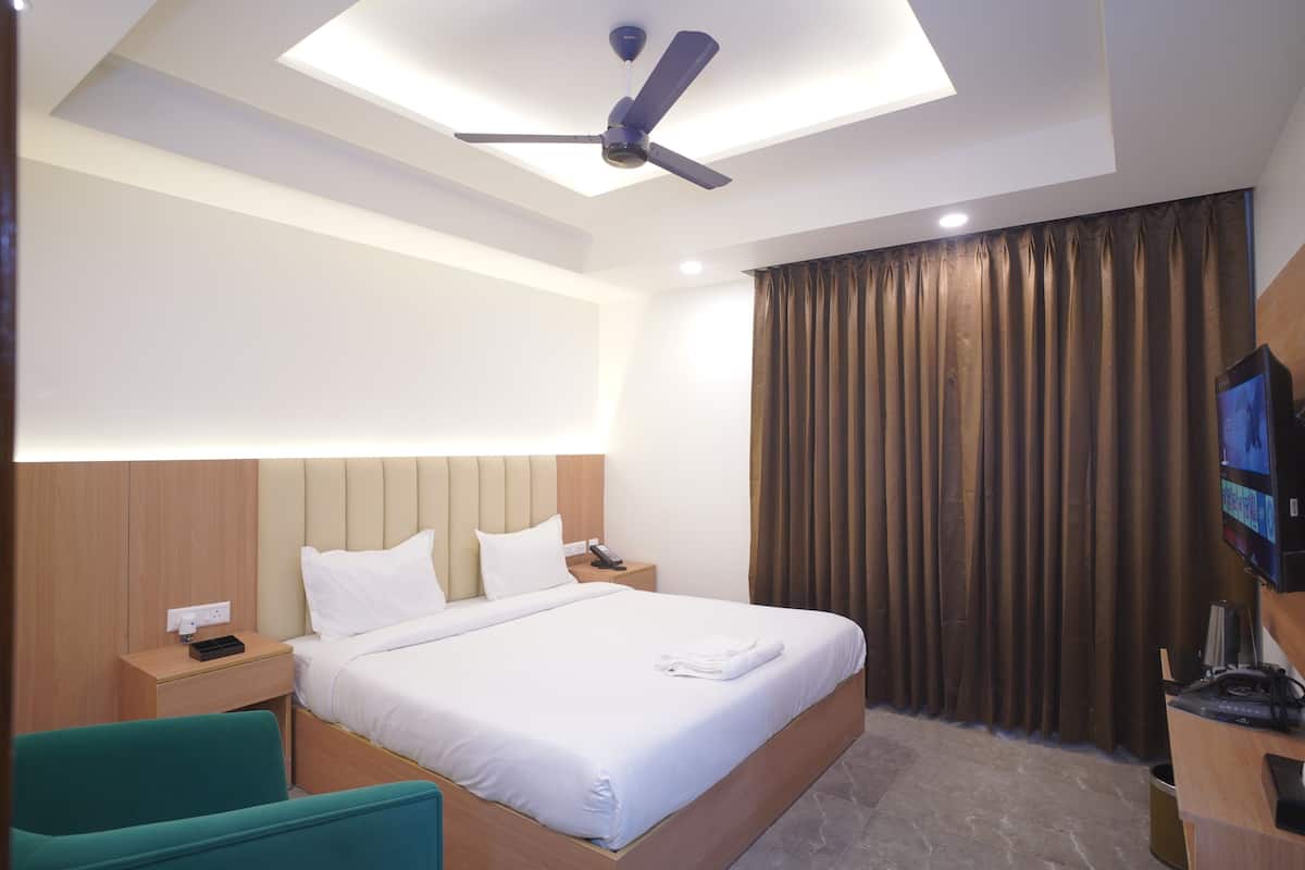 Une chambre d’hôtel équipée d’un lit, d’un bureau, d’une chaise, d’un ventilateur de plafond, d’une télévision et d’une fenêtre avec des rideaux.