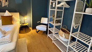 Une chambre à coucher comprenant un lit, une chaise, une étagère blanche et une petite table avec une lampe.