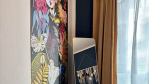 Ein Zimmer mit einem großen floralen Kunstwerk an der Wand, einem Bett mit weißem Kopfteil, einem Holzboden und einem Fenster mit beigen Vorhängen.