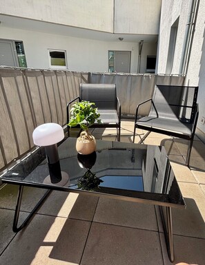 A glass-top table with a lamp and a bowl of nuts, two chairs, and a potted plant on a rooftop terrace.