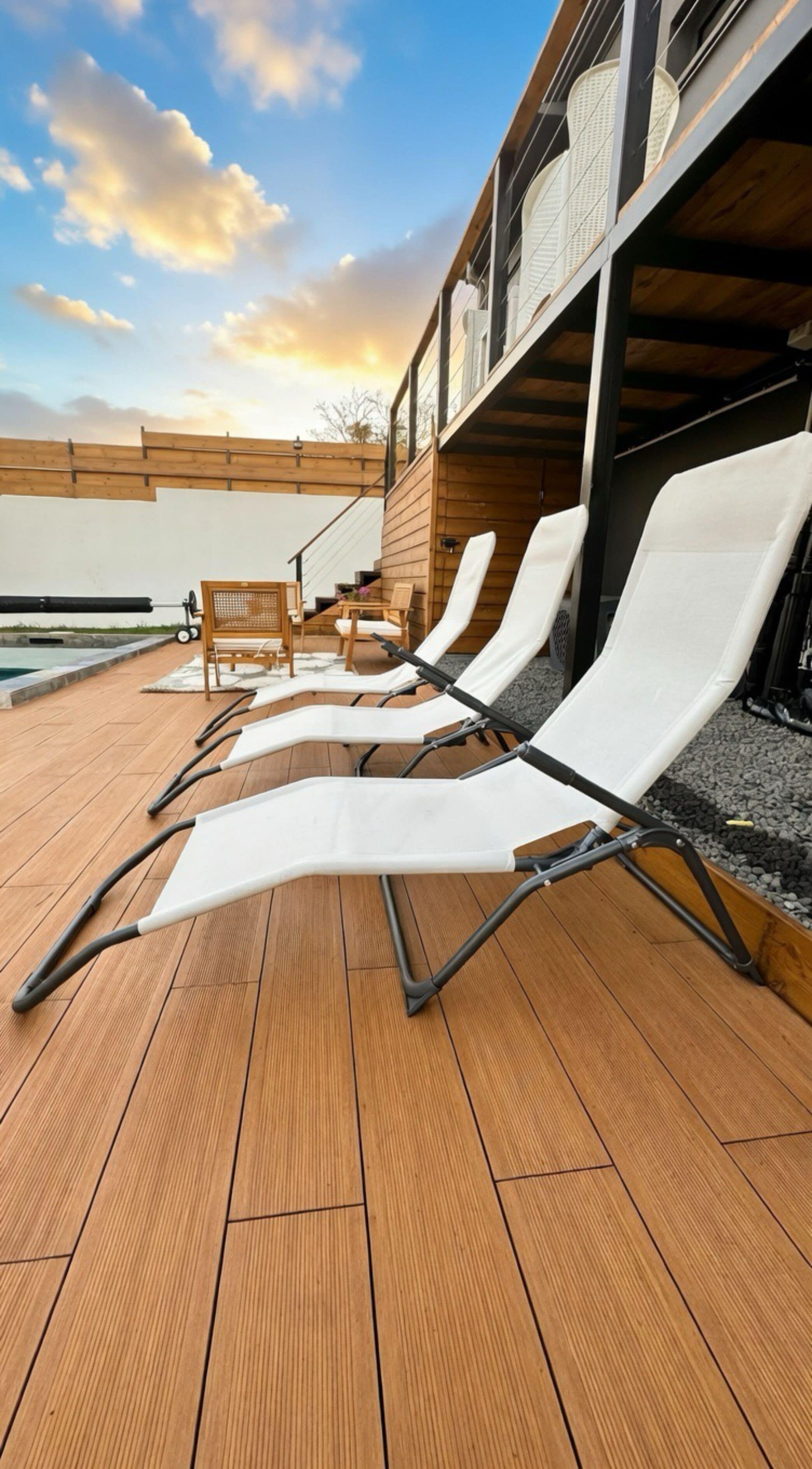 Une terrasse en bois avec des chaises longues, une petite table et une vue sur une piscine.