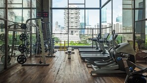 Une salle de sport équipée de machines de cardio, de matériel de musculation et de grandes fenêtres donnant sur la ville.
