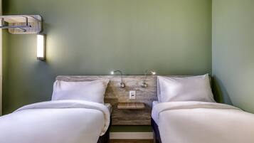Quarto com duas camas, cabeceira de madeira, luminárias de mesa e luminária fixa na parede.