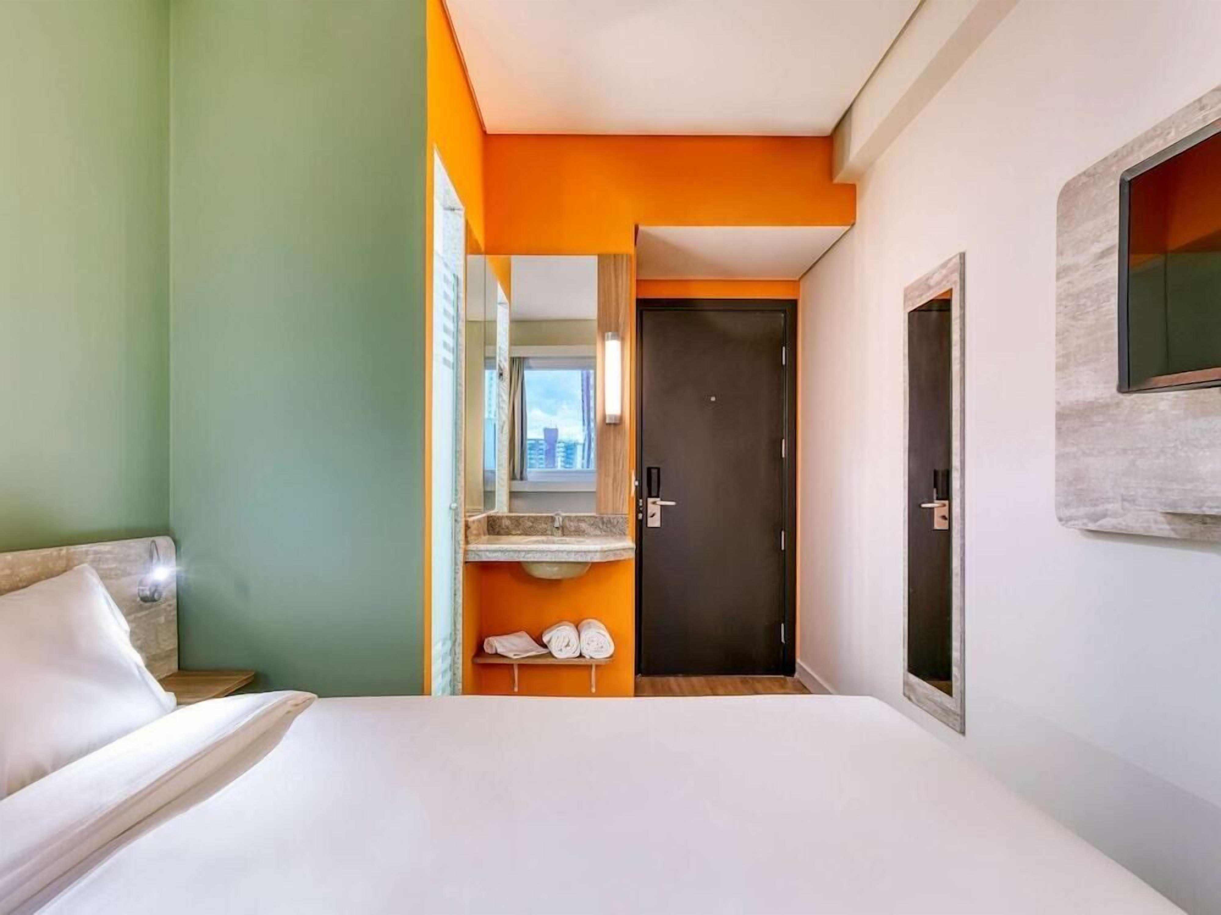 A hotel room with a bed, a bathroom with a mirror, and a door leading to another room.