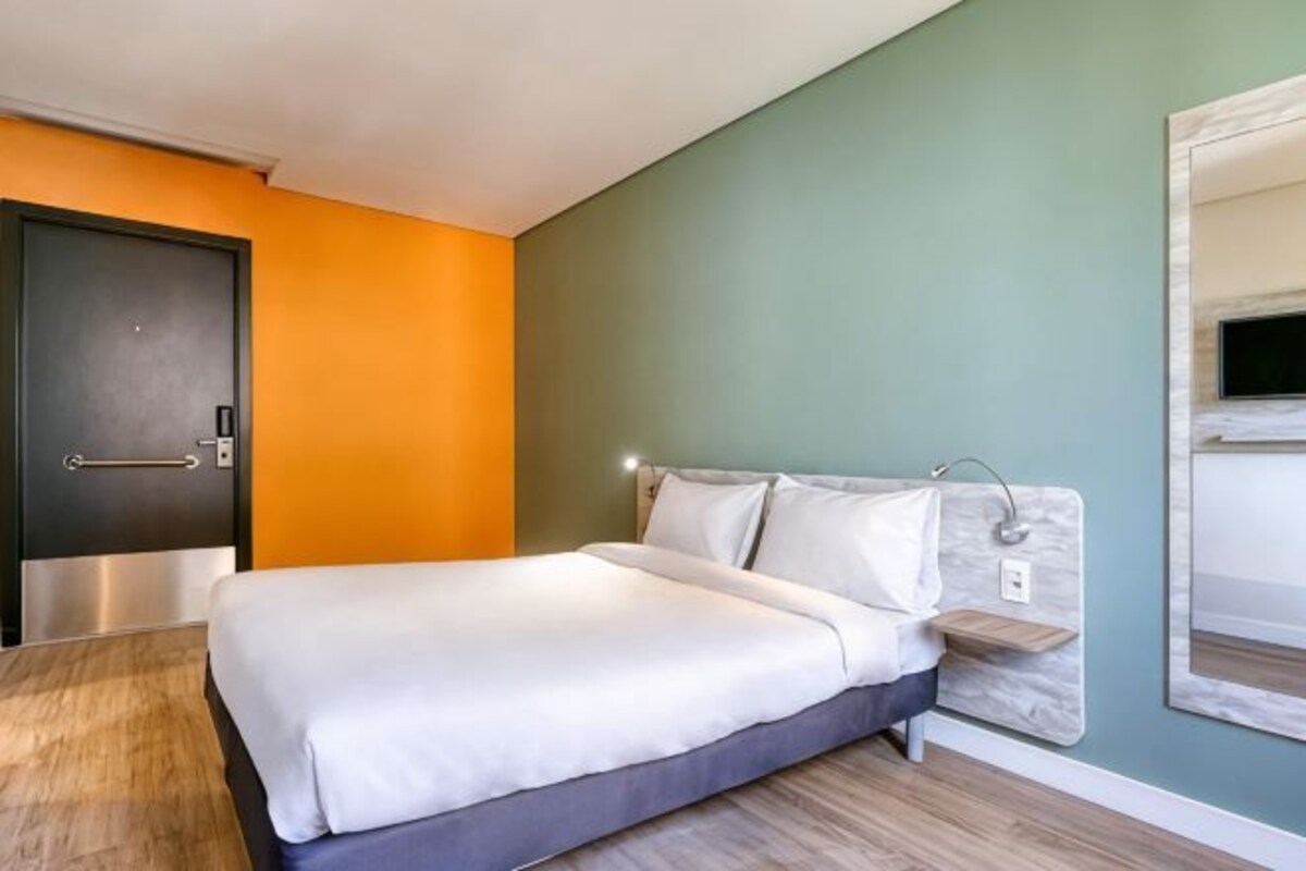Une chambre d’hôtel avec un lit, un plancher en bois, une porte et un téléviseur fixé au mur.