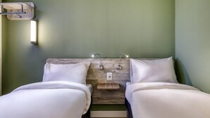 Una habitación con dos camas, cabecero de madera, lámparas de noche y una lámpara fijada a la pared.