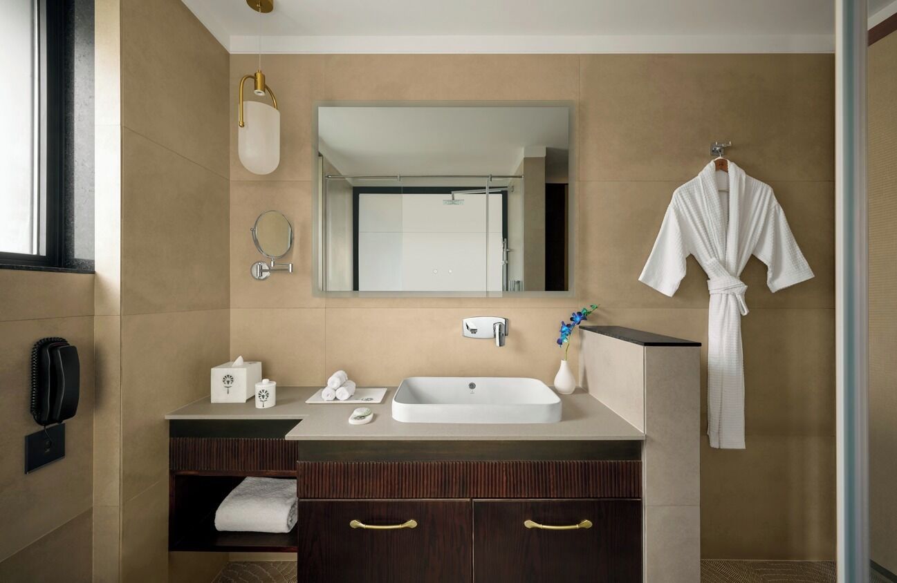 A modern bathroom with a large mirror, a white sink, and a robe hanging on the wall.