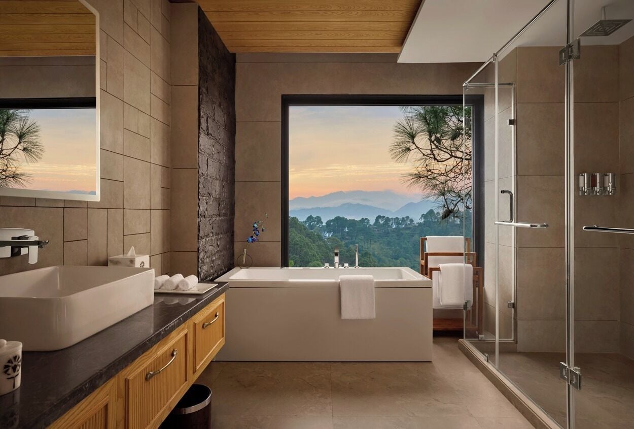 A modern bathroom with a large bathtub, a shower, and a view of mountains through a large window.