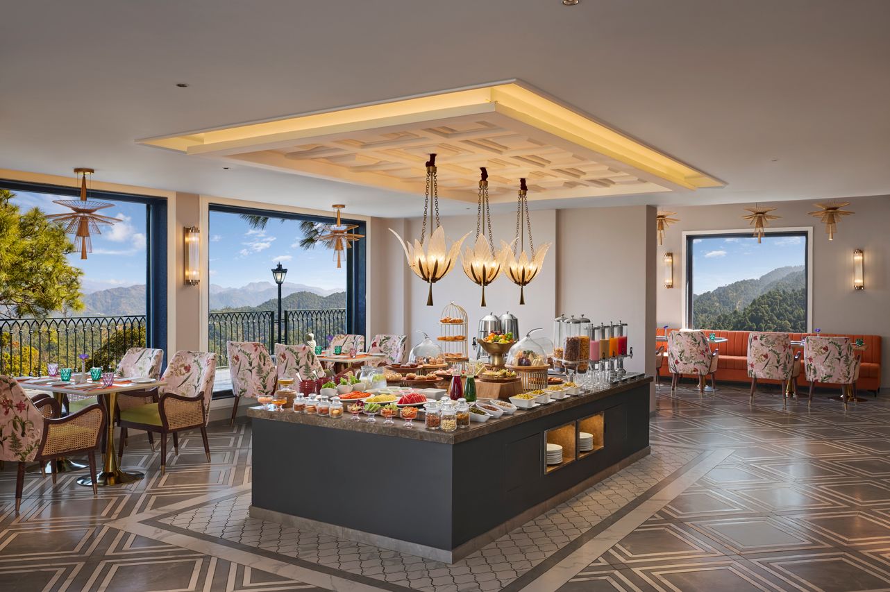 Un comedor de hotel con bufé, mesas y grandes ventanales con vistas a la montaña.