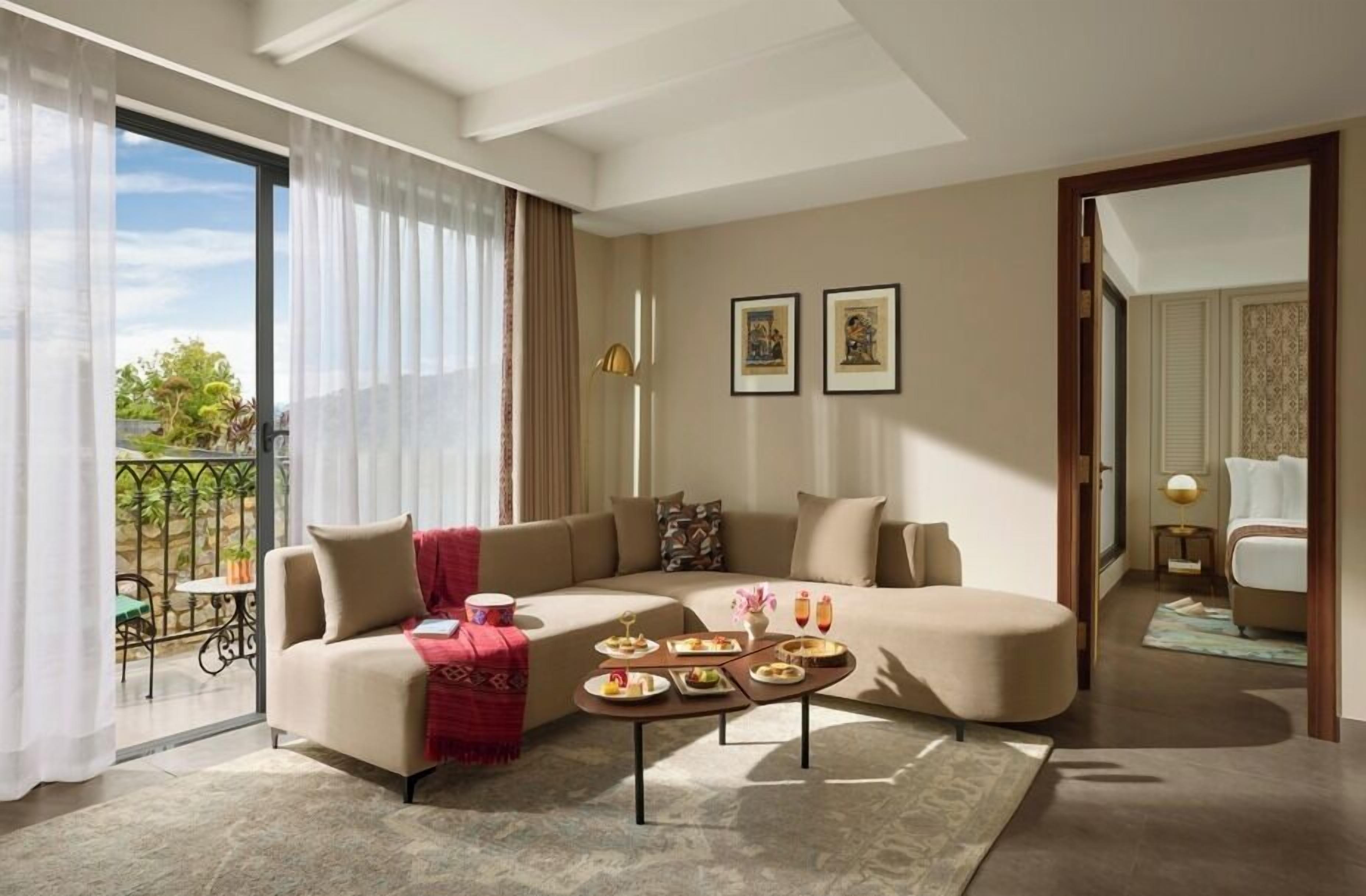 A modern living room with a sectional sofa, a coffee table with food, and a balcony with a view.