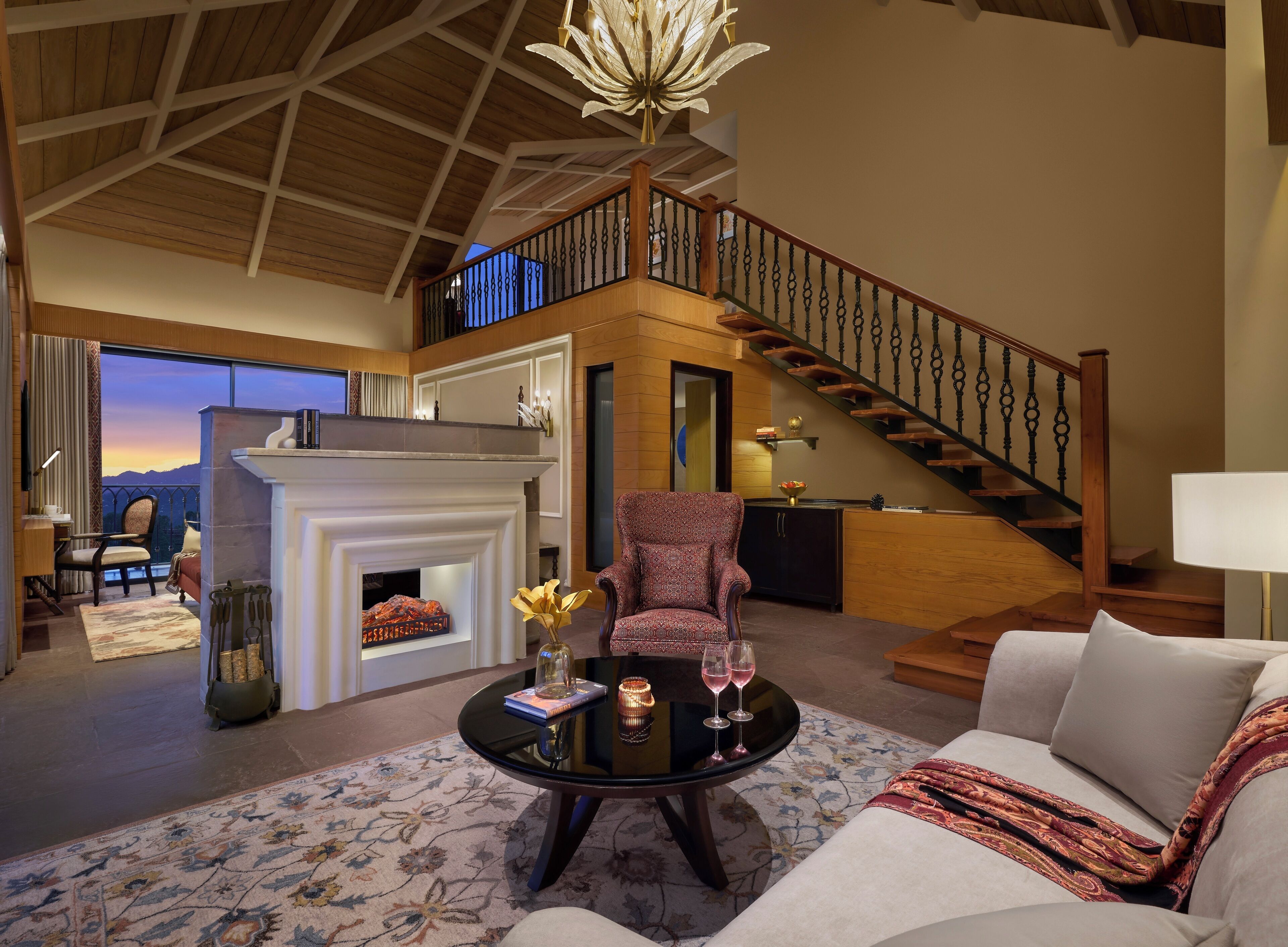 A spacious living room with a fireplace, a staircase, and a balcony with a view.