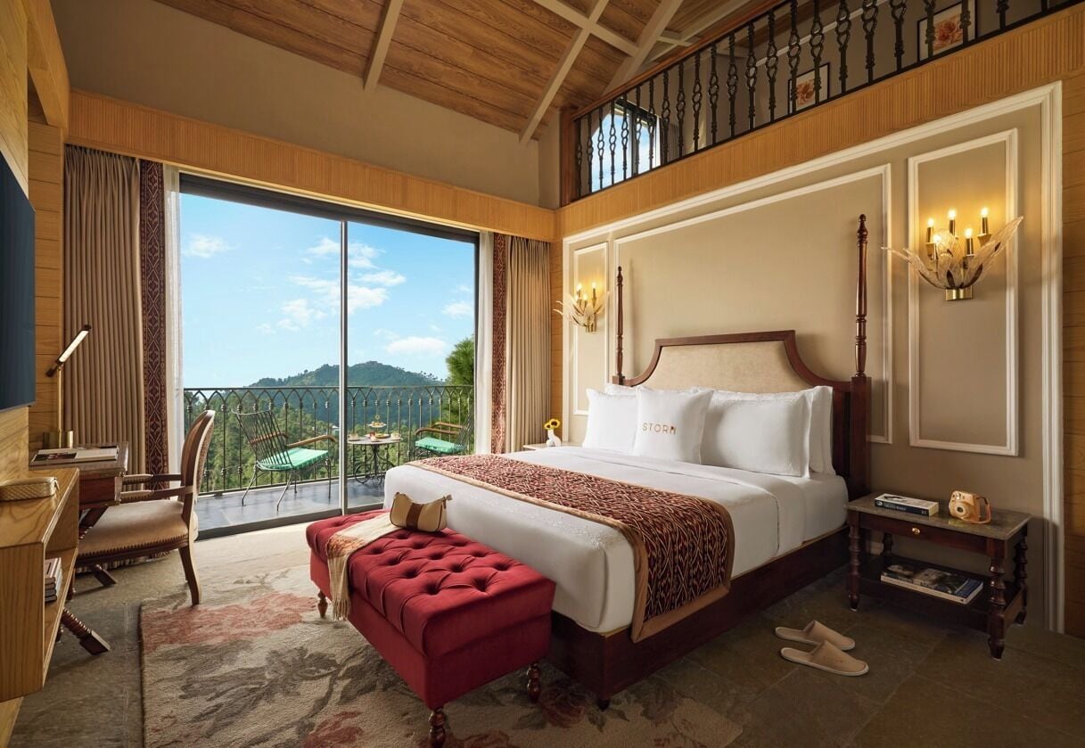Une chambre spacieuse avec un grand lit, un balcon offrant une belle vue, un bureau et un pouf rouge.
