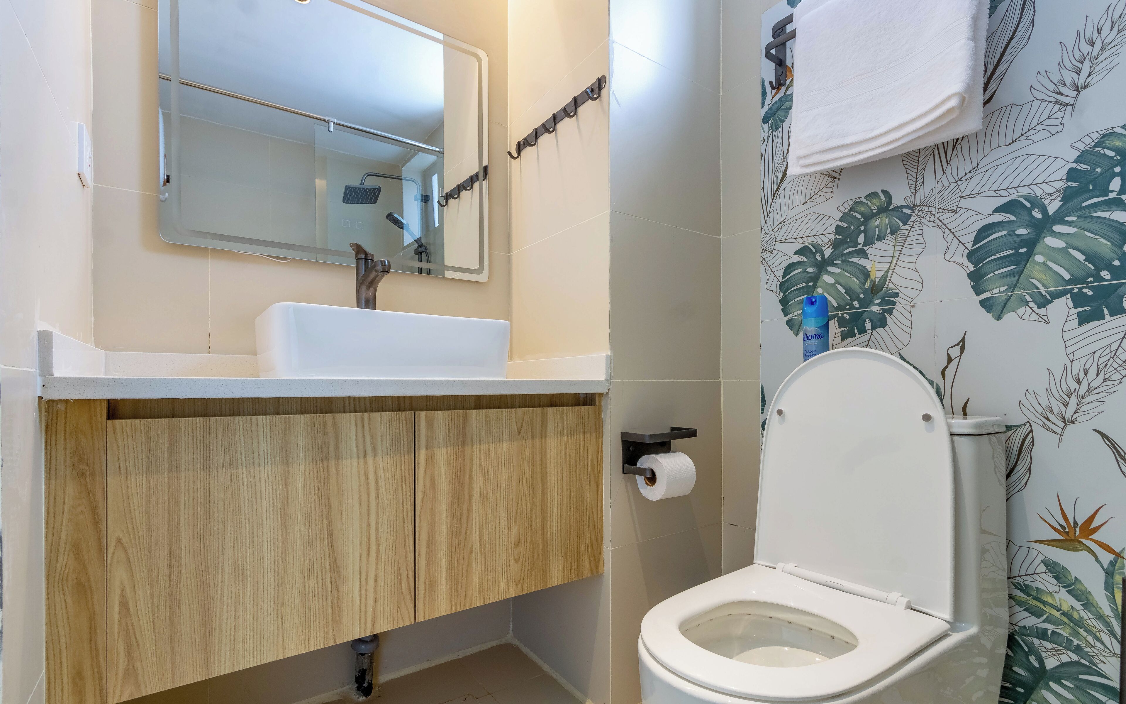 Un baño con lavamanos blanco, tocador de madera, inodoro y zona de ducha.