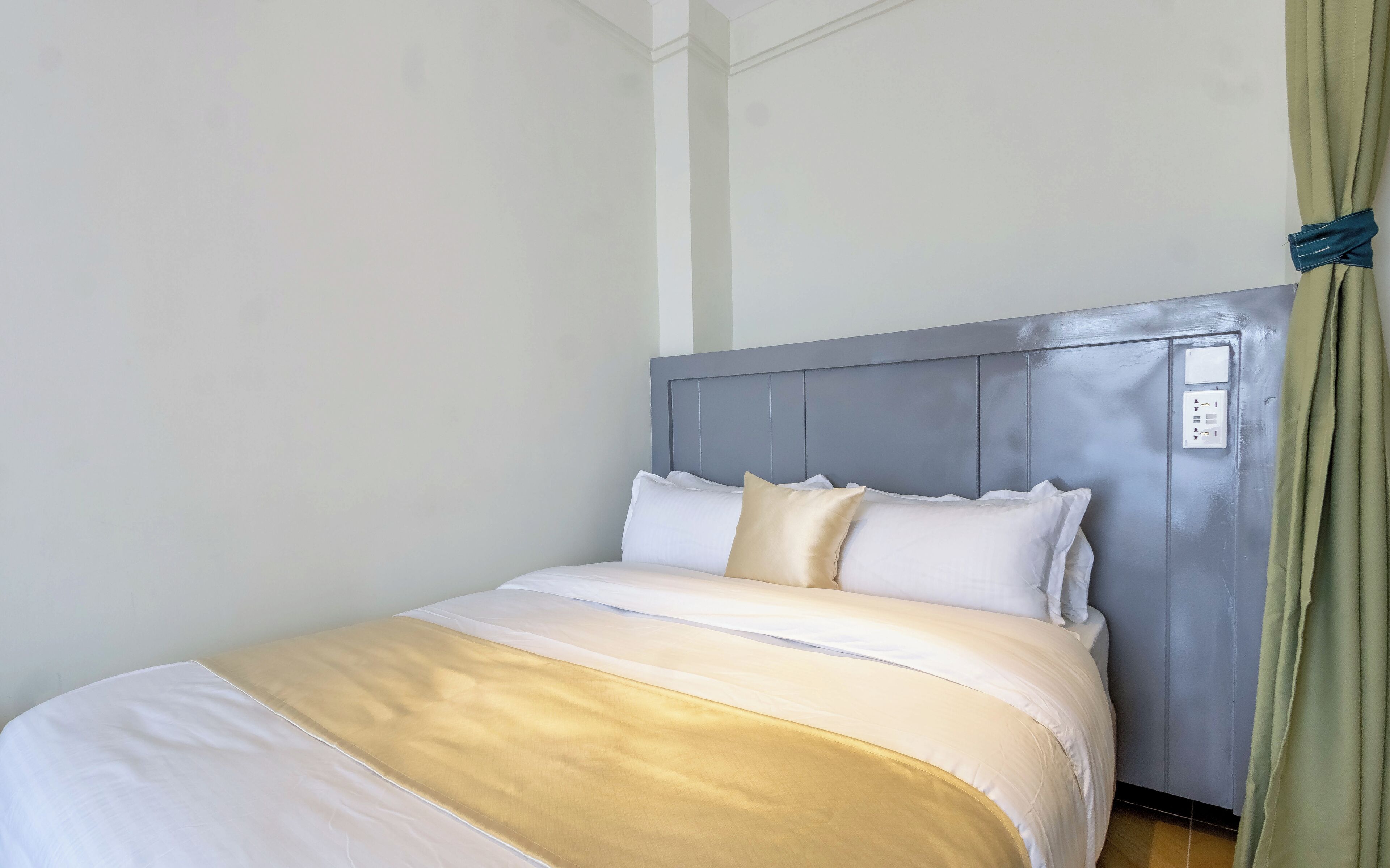 A neatly made bed with a grey headboard, white and beige bedding, and a power outlet on the headboard.