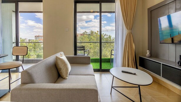 Un salon moderne avec un canapé, une petite table et un téléviseur. De grandes fenêtres offrent une vue sur l’extérieur.