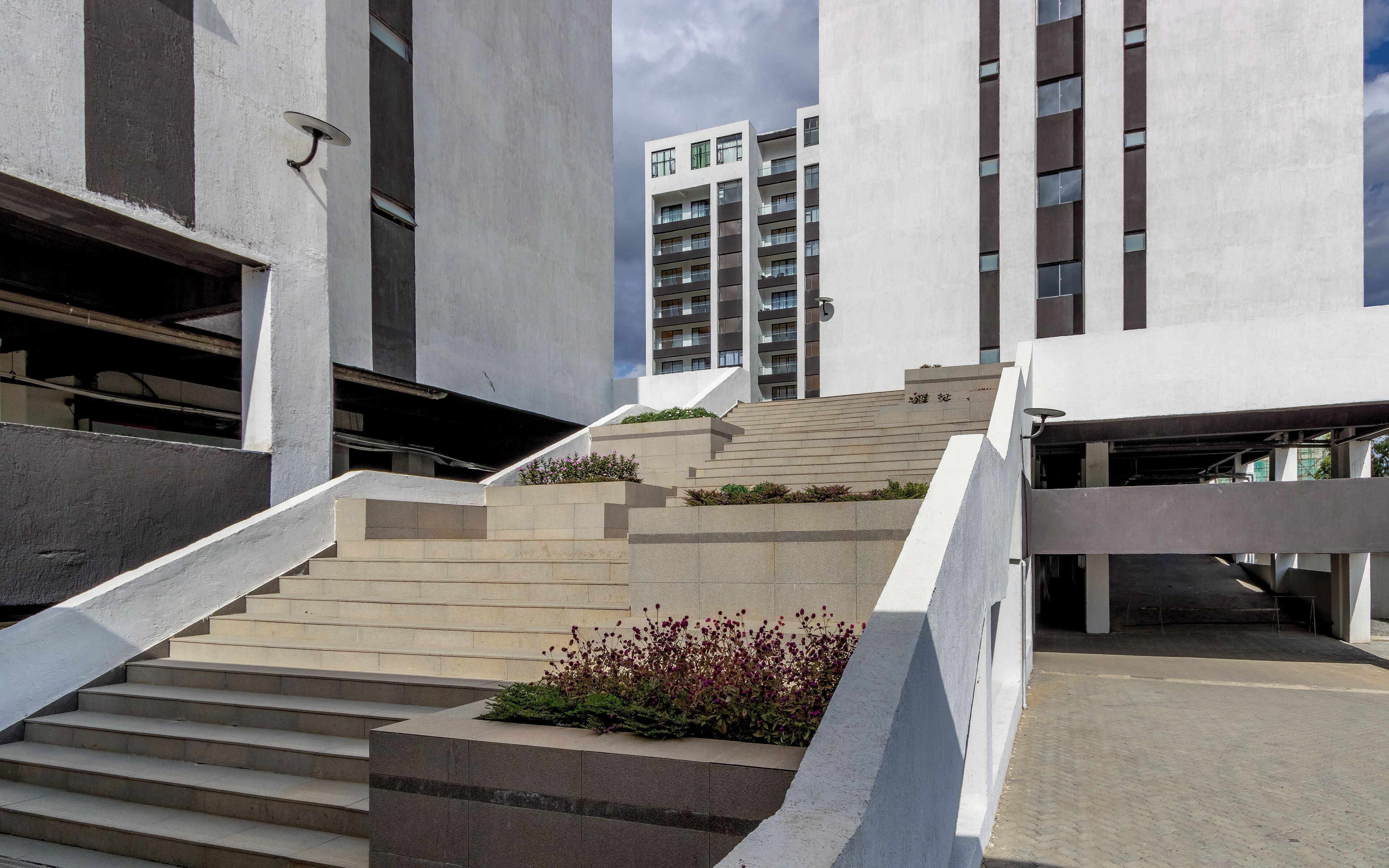 A modern building with a staircase leading to a higher floor, surrounded by concrete structures and a clear sky.
