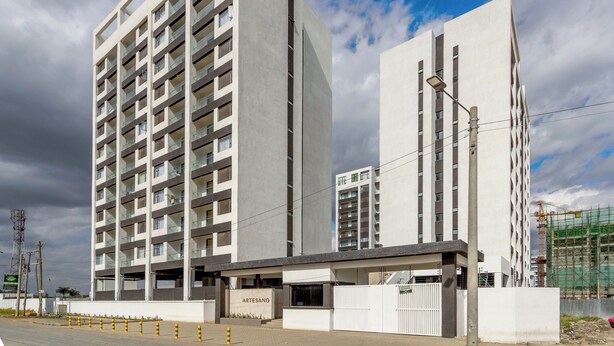 A modern building with multiple floors and balconies, a gated entrance, and construction scaffolding in the background. - JKIA luxury units (Syokimau)