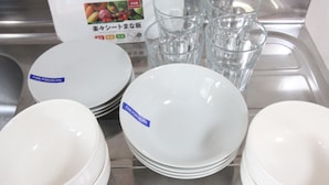 Ein Stapel weißer Keramikteller und -schüsseln mit dem Aufdruck 'FINE PORCELAIN' auf einer Edelstahl Arbeitsplatte.