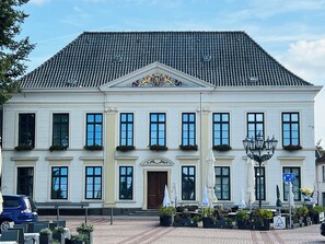 Ein weißes Gebäude mit einem Ziegeldach, großen Fenstern und einem zentralen Eingang mit einer Tür.